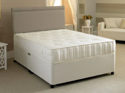 A large divan bed in a modestly decorated hotel room.